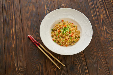 Fried rice with vegetables and beef in white plate, chopsticks on wooden background, Asian food concept, top view copy space