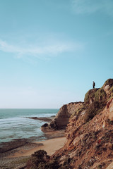 Man is standing on a cliff and looking at the sea to spot some waves. Sunny day.
