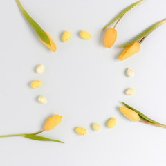 Wreath made of yellow easter eggs and flowers on a blue pastel background. Greeting card concept with place for text.