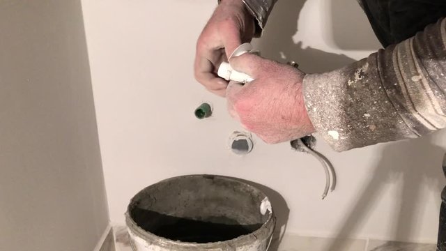 Construction worker taping faucet spigot with fresh whitewash wall paint background in 4k