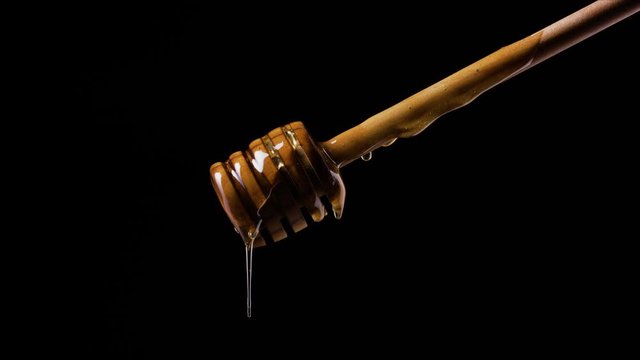 Honey on dipper in front of black background