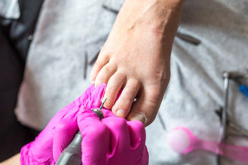 Pedicurist master in pink gloves cuts the cuticle and shellac toe nails in the pedicure salon using drill.  Professional pedicure in cosmetology clinic. Hygiene for feet in beauty salon.