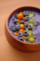 Smoothies of violet color from banana and currant, on top of a blackberry, physalis and kiwi berry. Smoothies in a wooden bowl.