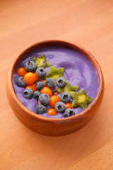 Smoothies of violet color from banana and currant, on top of a blackberry, physalis and kiwi berry. Smoothies in a wooden bowl.