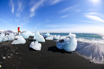 A man on a block of ice on the black volcanic sand on the 