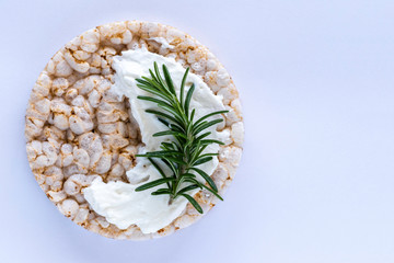 Crispy rice round bread with cream cheese and  fresh rosemary on soft blue background with copy space.