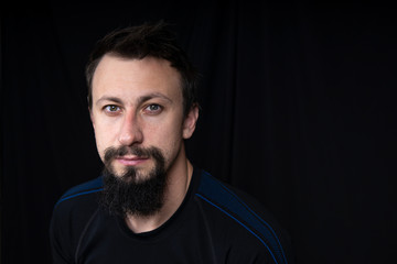 Obraz premium a close up portrait of a young man with beard in dark clothes on a dark background