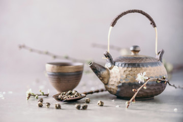 Black and brown iron teapot and tea cups, blossom flowers cherry branch on gray background. Top...