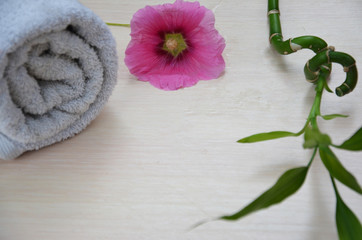 background of a spa with pink flower, white towel rolled up and a sprig of green bamboo