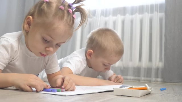 happy family brother and sister teamwork concept. little boy and girl draw on floor in a sketchbook. brother and sister in the room lifestyle draw with crayons