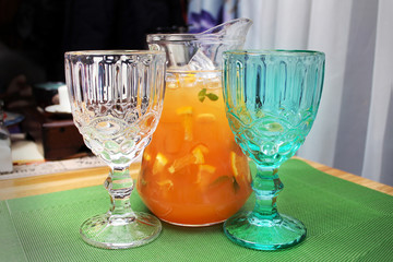 Jug with orange juice and two glasses near - white and green on a table in a restaurant