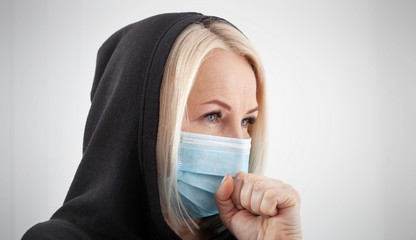 Woman wearing face mask. Woman with flu sneezing, a woman in a hoodie in winter clothing wearing mask to her nose in a cold and flu health concept against air pollution background.