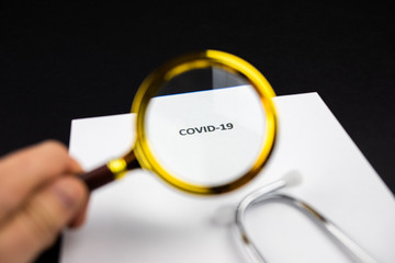 Pandemia COVID-19, napis powiększony przez lupe, strzykawka, stetoskop na ciemnym tle