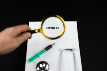 Pandemia COVID-19, napis powiększony przez lupe, strzykawka, stetoskop na ciemnym tle - obrazy, fototapety, plakaty