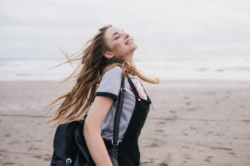 Romantic long-haired woman with black backpack enjoying good day at sandy beach. Outdoor shot of...