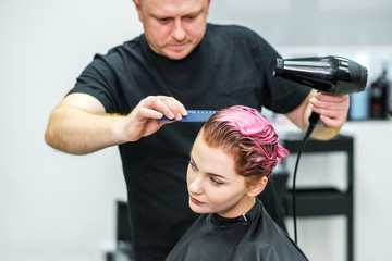 Hairstylist dries hair of woman.