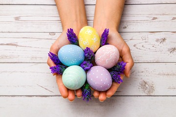 easter concept. closeup beautiful woman hands holding hand-painted easter eggs in tender pastel colors and lavender flowers over wooden table