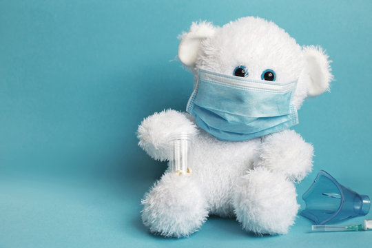 big teddy toy bear are sitting in white medical mask with mask for inhalation, syringe and tablets on a blue background.