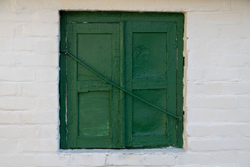 Old green window with peeling paint on a white brick wall.