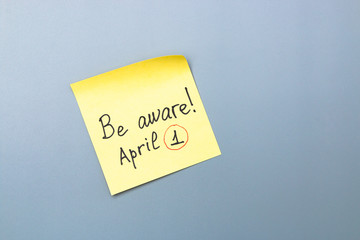 be aware on yellow sticky note over a grey background. april fools day