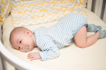 The baby lies in a crib on his tummy.