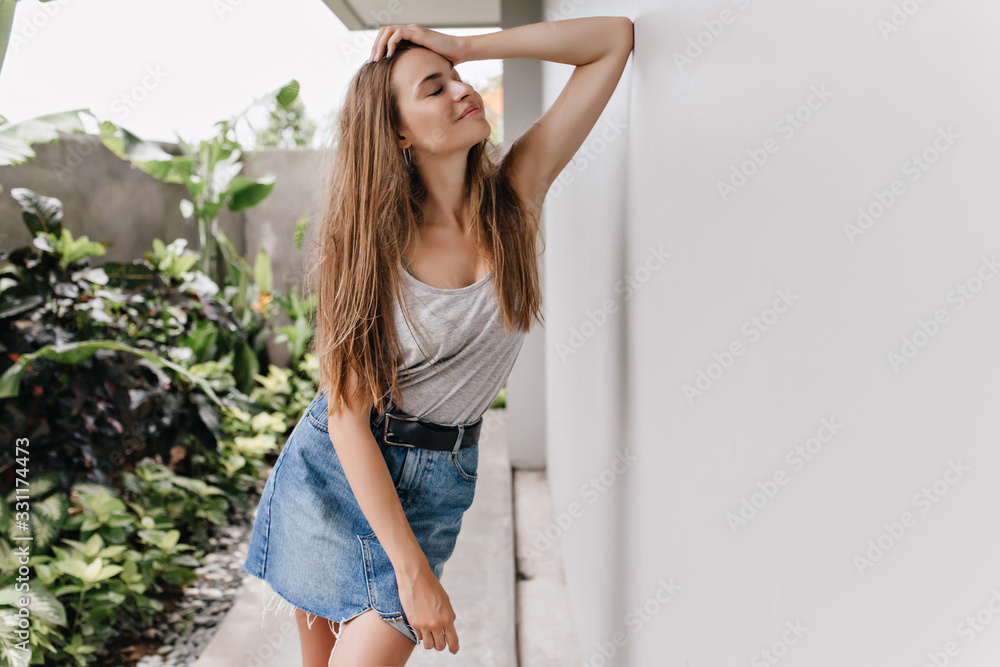 Wall mural stunning slim girl posing near plants with inspired face expression. magnificent lady in retro denim