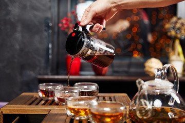 glass teapot with tea and cups stand on a wooden stand, pouring a drink
