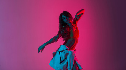 Sexy pretty young woman dancer in stylish youth clothes dancing and posing in a room with bright neon blue-pink color. Sports girl enjoys a dance in the studio with multi-colored ultraviolet light.