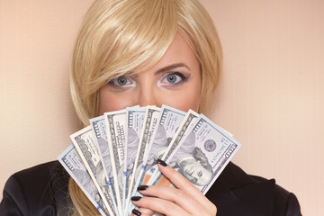 Attractive blonde woman is holding dollar bills in her hands. Pink background.