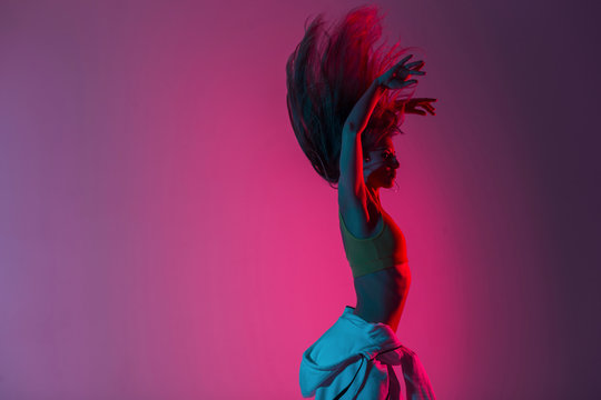 Modern Young Woman In Fashionable Clothes Dancing In Studio With Pink Color Background. Beautiful Trendy Girl The Dancer Enjoys Dancing In The Room With Colored Light In Style Disco. Art Dance Concept