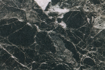 Texture of black marble with white lines of a pattern, macro background. Dark gray stone backdrop from mineral tile
