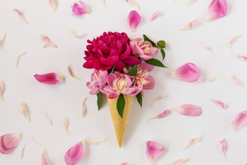 Beautiful creative flat lay with flower ice cream - fresh bright pink peonies in a waffle cone on a white background strewn with many soft pink petals. Mother's Day celebration concept. Close up
