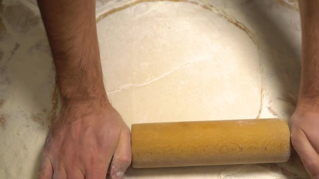 TOP VIEW: Male hand rolled fresh dough on the table with the help of a rolling pin. Man rolls dough with rolling pin for pita breads. Fresh flour is scattered around. Fresh dough for the pie. Close up
