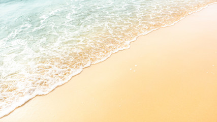 Golden brown sand on a beach with white foam on wave of pastel green color sea water