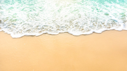 Golden brown sand on a beach with white foam on wave of pastel green color sea water