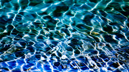 Dark blue transparent water with sunlight reflections texture background.