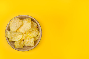 Patatas fritas onduladas en un bol de madera sobre un fondo liso amarillo brillante. Vista superior y de cerca. Copy space
