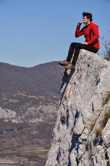 Young man resting on a cliff with a gorgeous view. Concept of freedom. Man eating on a cliff edge