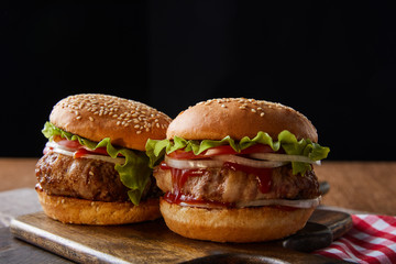 two burgers on wooden cutting boards isolated on black