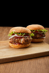 two tasty burgers on wooden cutting board isolated on black