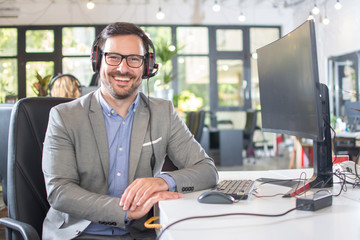 Cheerful male technical support operator with headset working in call centre