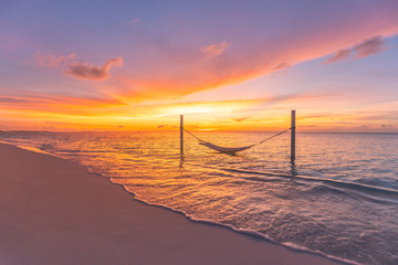 Beautiful landscape on sunset beach, orange evening as luxury travel background. Amazing sunset colors, soft waves on empty beach with swing or hammock. Summer landscape, tropical sunset on vacation