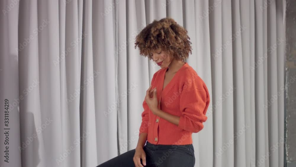 Wall mural Mixed race woman on grey curtains background sits on chair and dancing with hand lifted up