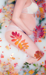 pregnant woman lies in a milk bath with leaves and rowan berries