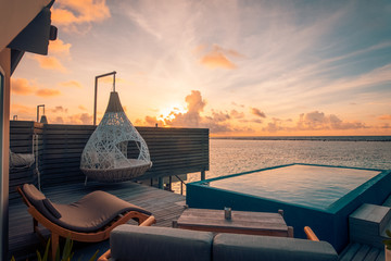 Beautiful swing sofa on the infinity swimming pool waters outdoor beach with colorful sunset sky....