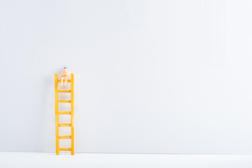 Doll on ladder on white surface on grey background, concept of equality rights