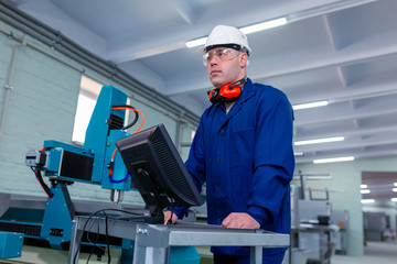 Naklejka na ściany i meble CNC machine operator in the Hard white Hat Walks Through Light Modern Factory While Holding tablet. Successful, Handsome Man in Modern Industrial Environment.