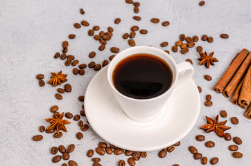 A cup of black aromatic coffee in a white cup with anise stars and cinnamon sticks on a softer background