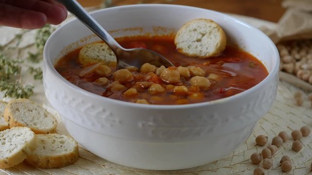 Healthy eating, take tablespoon chickpeas soup with tomatoes in a bowl. On the table a bowl of creamy and rustic legume soup. Eating healthy vegetarian dinner. Cozy and warm food. Protein dinner.
