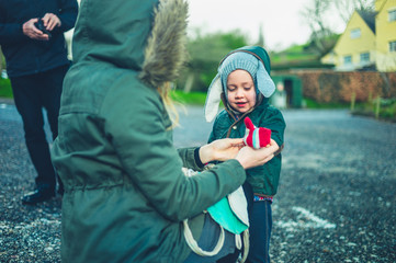 Mother helping her preschooler put on his gloves outdoors in winter - obrazy, fototapety, plakaty